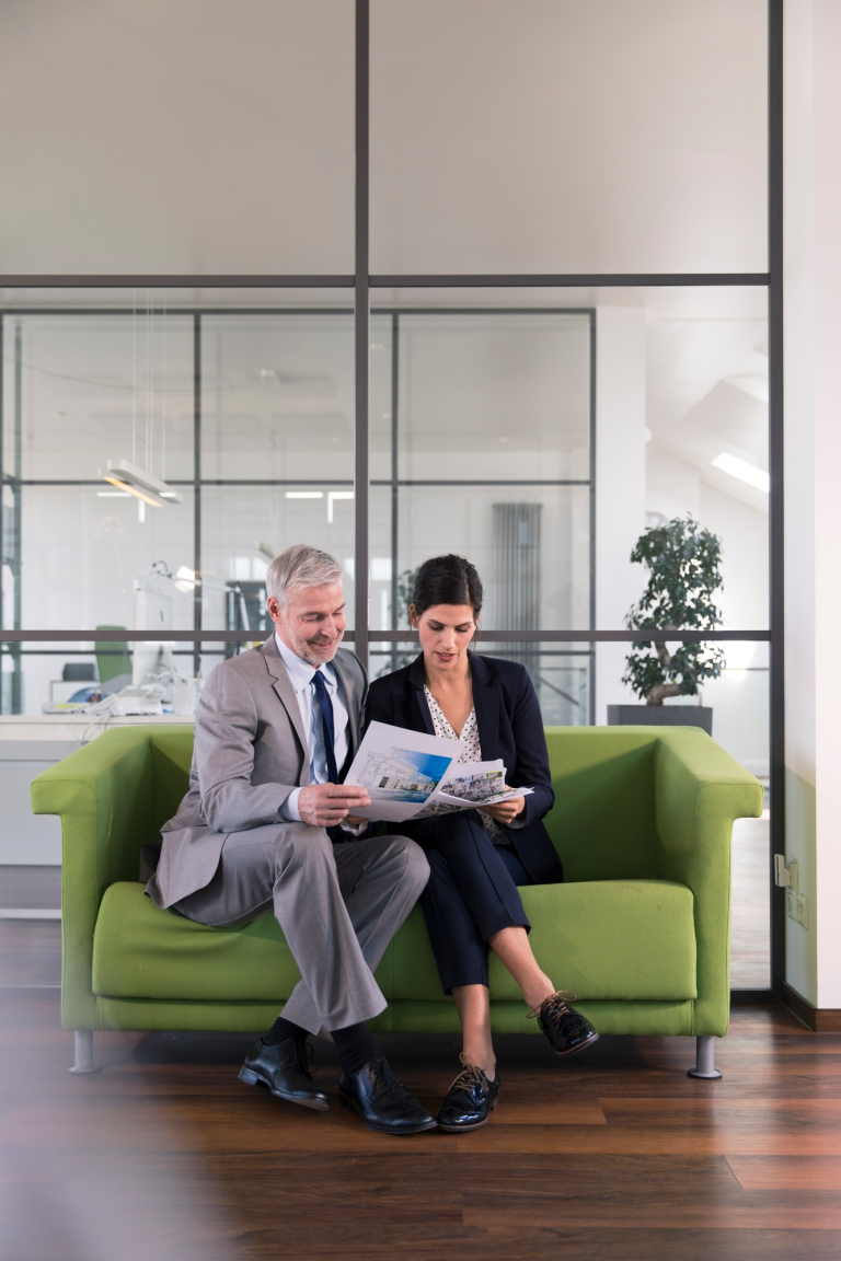 businessman-and-woman-sitting-on-couch-in-office-looking-at-documents